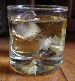 A photo of a glass of scotch set on a wooden table