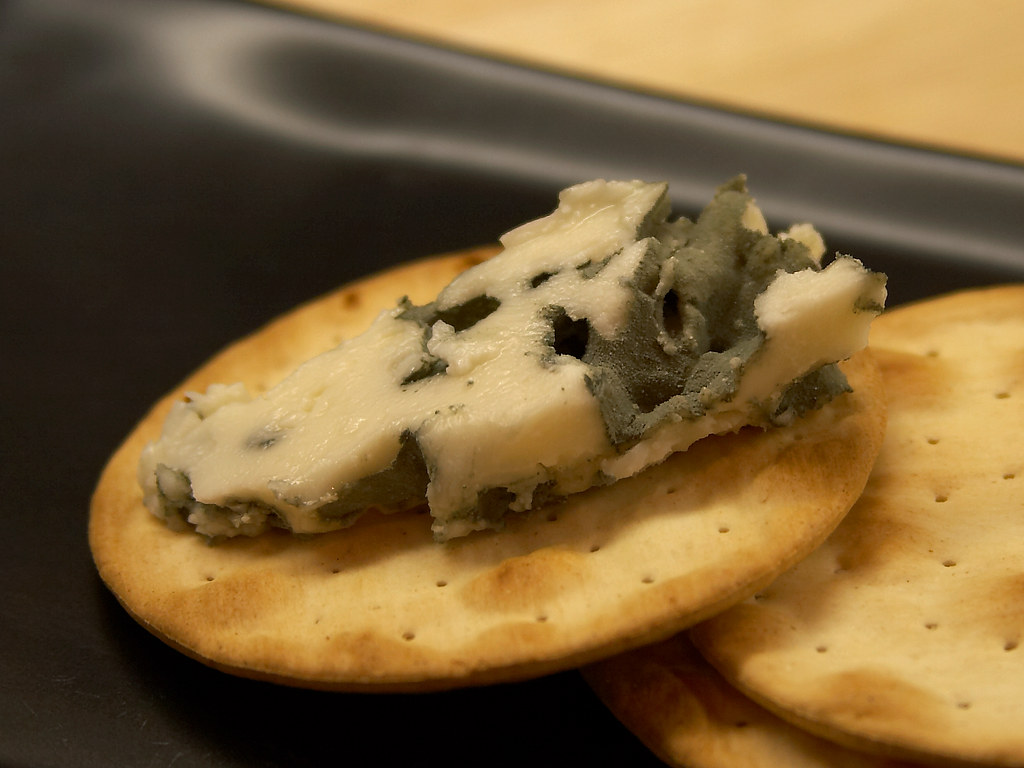 A close-up photo of Roquefort cheese (colloquially 'blue cheese') spread across a round cracker