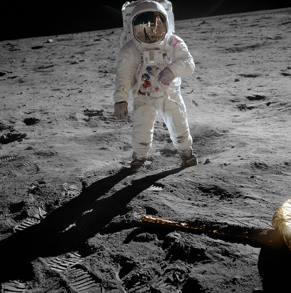 A photograph of astronaut Buzz Aldrin in his spacesuit on the moon. His helmet visor reflects the Apollo 11 lander and Neil Armstrong, who is taking the photo.