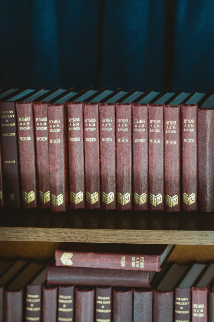 A photo of red and black hardbound books on a brown wooden shelf by Annie Spratt