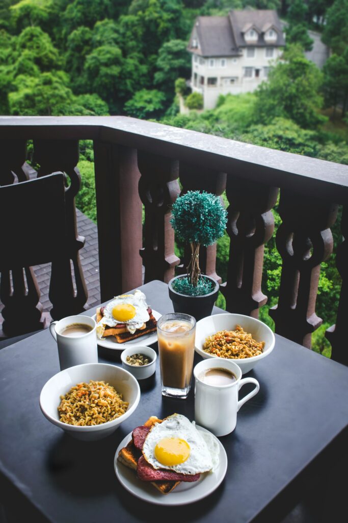 A photo of breakfast for two on a table on a patio. Each person has a plate with toast, spam, an egg, and a bowl of rice, with mug of coffee next to each.