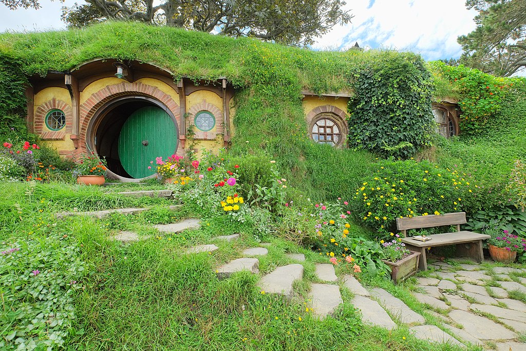 Baggins residence 'Bag End' with round green entrance door ajar (Hobbiton movie set); the tree above is artificial, fabricated complete with countless metal leaves - the location needed a tree above the hobbit hole, but there was none, so a tree was "created" instead.